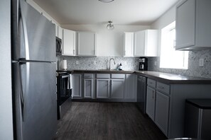 Una cocina moderna con armarios blancos, un refrigerador de acero inoxidable, un horno empotrado y un microondas.