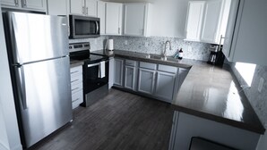 Een moderne keuken met witte kastjes, roestvrijstalen apparatuur, een granieten aanrechtblad en een houten vloer.