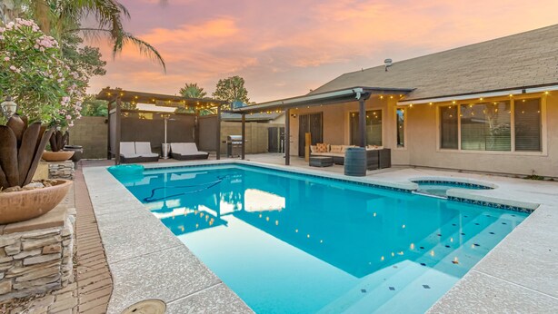 A swimming pool with lounge chairs and a covered seating area, surrounded by a house with a stone facade and a clear sky. - Experience Deer Valley charm, just 14 mins from Grand Canyon University (Phoenix)