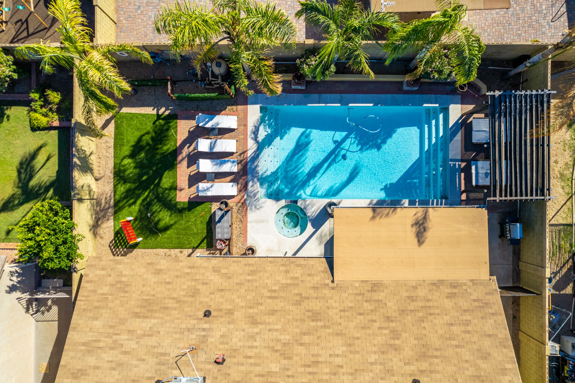 An aerial view of a rooftop pool area with a pool, sun loungers, and palm trees.