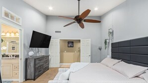 A bedroom with a bed, a ceiling fan, a TV, and a bathroom visible through an open door. - Experience Deer Valley charm, just 14 mins from Grand Canyon University (Phoenix)