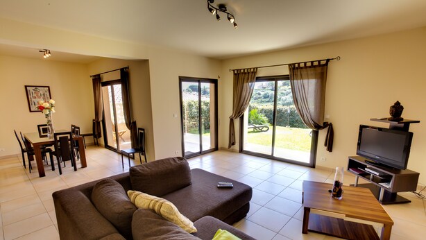 A living room with a sofa, TV, and a dining area with chairs and a table.