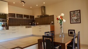 A modern kitchen with a dining area, featuring a large table, chairs, a vase with flowers, and a painting on the wall.
