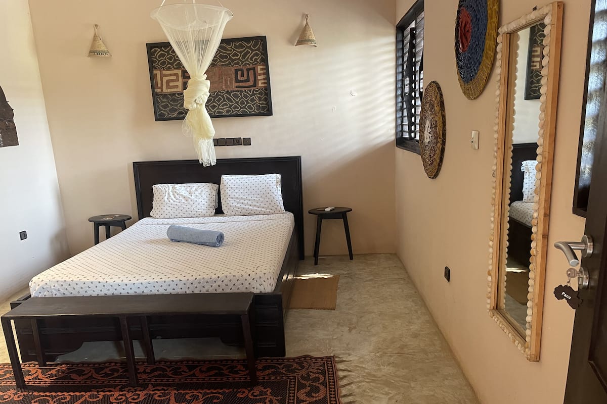 A neatly arranged bedroom with a bed, bedside tables, a hanging mosquito net, and decorative wall art.