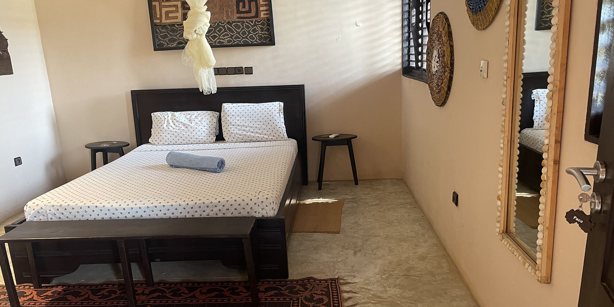 Un dormitorio pequeño y ordenado con cama, mesitas de noche, una lámpara colgante y un espejo.