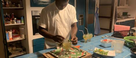 Un chef preparando una bebida en una cocina con paredes azules, una estufa y diversos utensilios sobre la encimera.