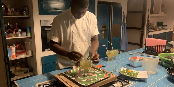A chef preparing a drink in a kitchen with blue walls, a stove, and various kitchen items on the counter. - La Maison Bleue Lomé (Lomé)
