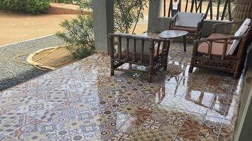 Un patio techado con baldosas estampadas, muebles de mimbre y una manguera en el suelo.