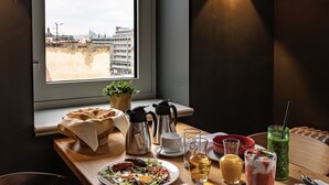 A breakfast table with a variety of food and drinks, a window with a view of buildings, and a wall-mounted light fixture. - The Viaduct Suites & More (Prague)