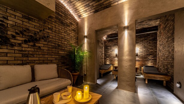 A spa room with a brick wall, a wooden bench, a sofa, and a table with candles. - The Viaduct Suites & More (Prague)