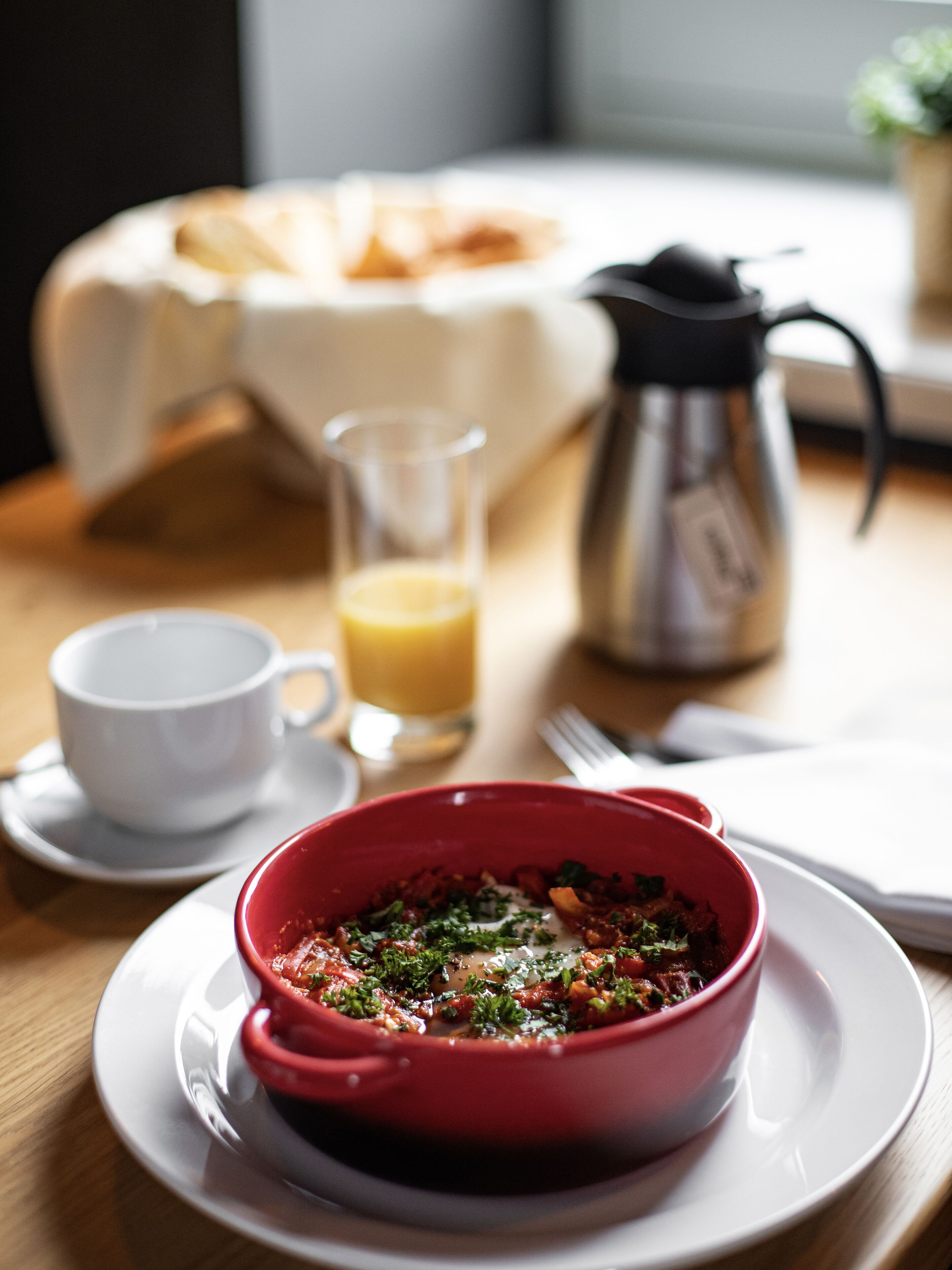 Una mesa de comedor con un tazón rojo de comida, una taza de café, un vaso de jugo de naranja y una cafetera.