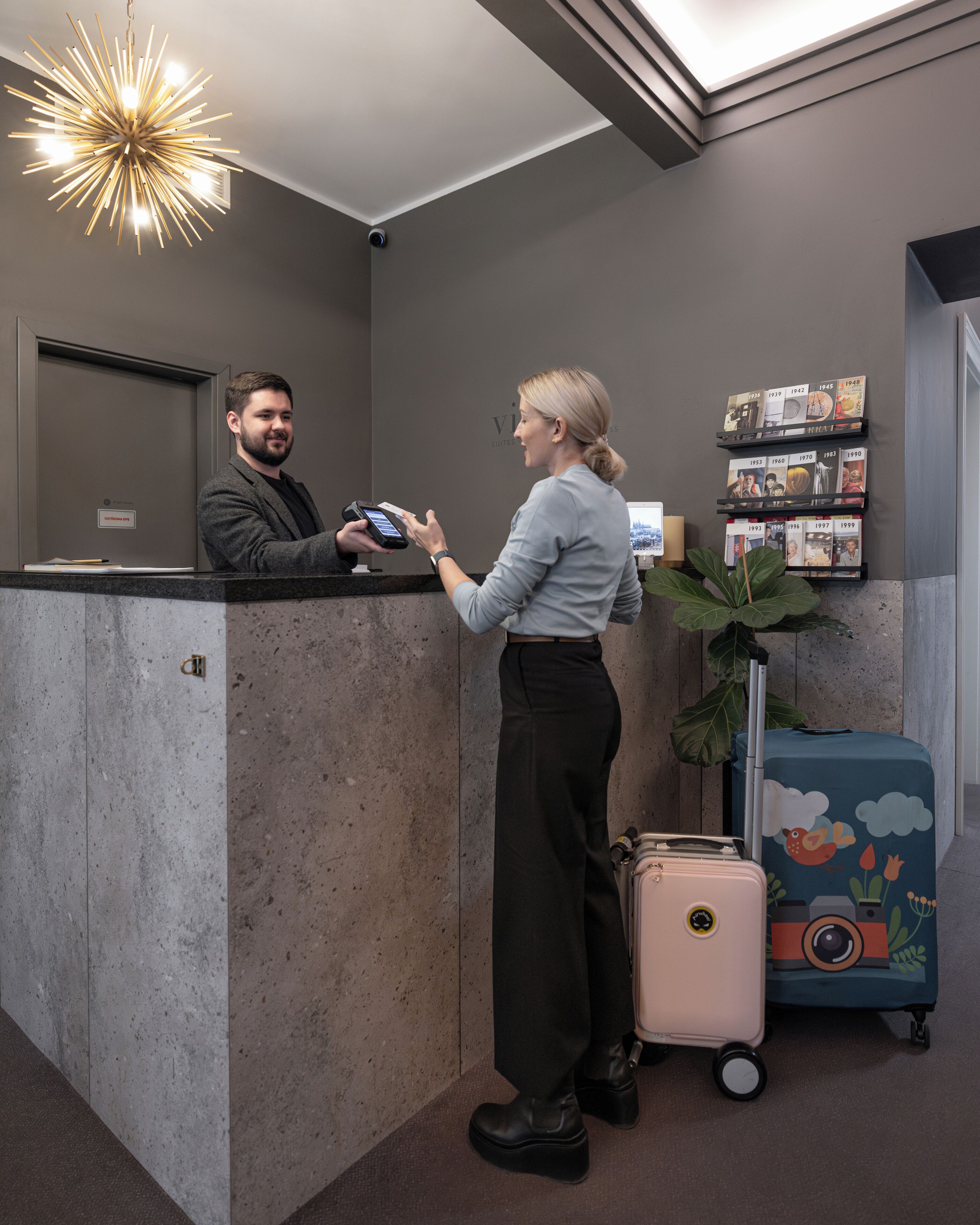 A reception desk with a modern chandelier, a digital display, and a wall-mounted photo display.