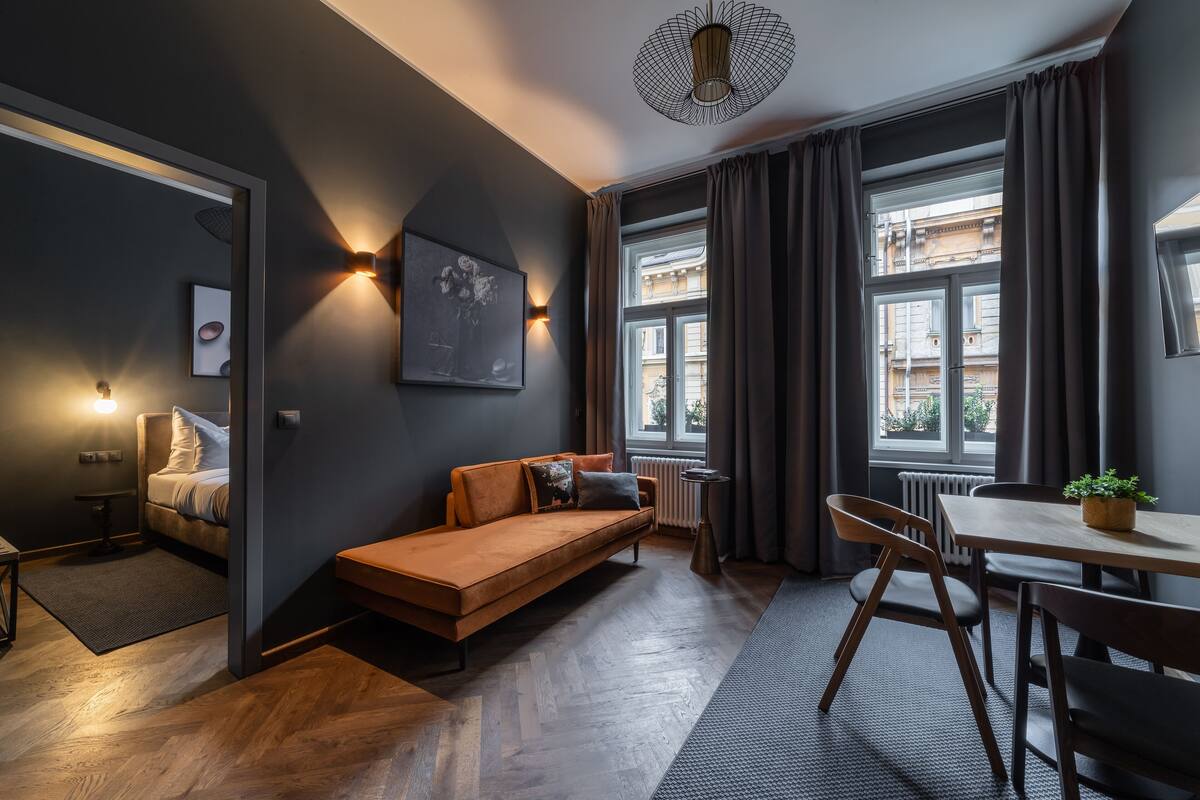 A modern living room with a sofa, a dining table, and a view of the city through large windows.