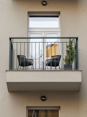 Un balcón con dos sillas, una planta en maceta y una ventana.