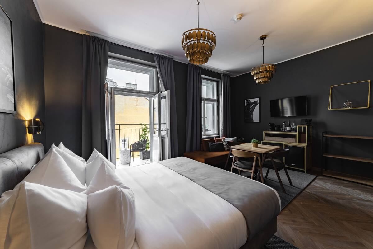 A modern hotel room with a large bed, a desk, a TV, and a balcony.