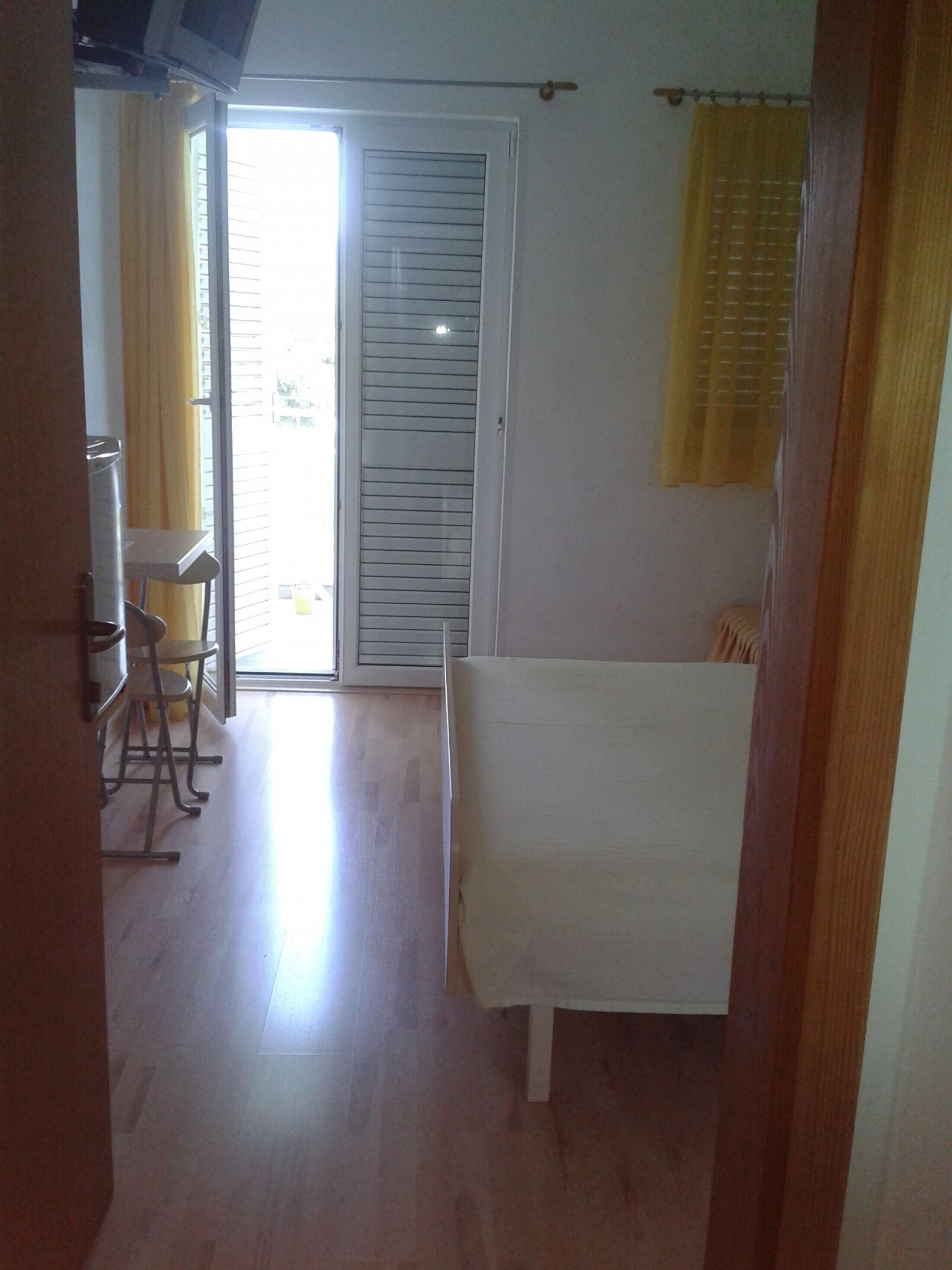 Quarto com cama, cadeira, mesa e porta de correr que dá para área externa.