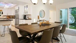 Une cuisine moderne avec des meubles blancs, un réfrigérateur en acier inoxydable et un coin repas comprenant une table et des chaises en bois.