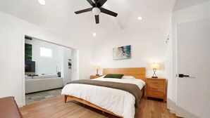 Une chambre moderne avec un lit en bois, deux tables de chevet avec des lampes, un ventilateur de plafond et une grande fenêtre.