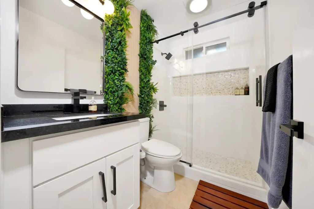 Ein modernes Badezimmer mit Waschbecken in Weiß, einer schwarzen Arbeitsplatte, einer weißen Toilette und einer Duschkabine aus Glas.