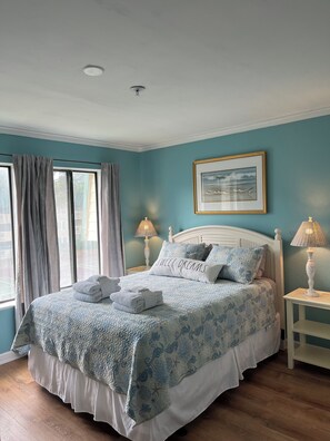 A neatly made bed with a blue and white patterned bedspread, a pillow with "SWEET DREAMS" text, and a framed seagull picture on the wall.