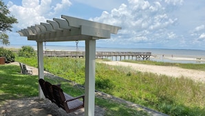 A wooden bench under a white pergola overlooking a beach with a wooden pier in the background. - Peaceful 2BR Beach Condo with Pools, Tennis, Pickleball, Sauna, Gym & More! (Hilton Head Island)