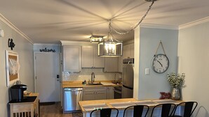 A modern kitchen with stainless steel appliances, a wooden island with bar stools, and a welcoming sign. - Peaceful 2BR Beach Condo with Pools, Tennis, Pickleball, Sauna, Gym & More! (Hilton Head Island)