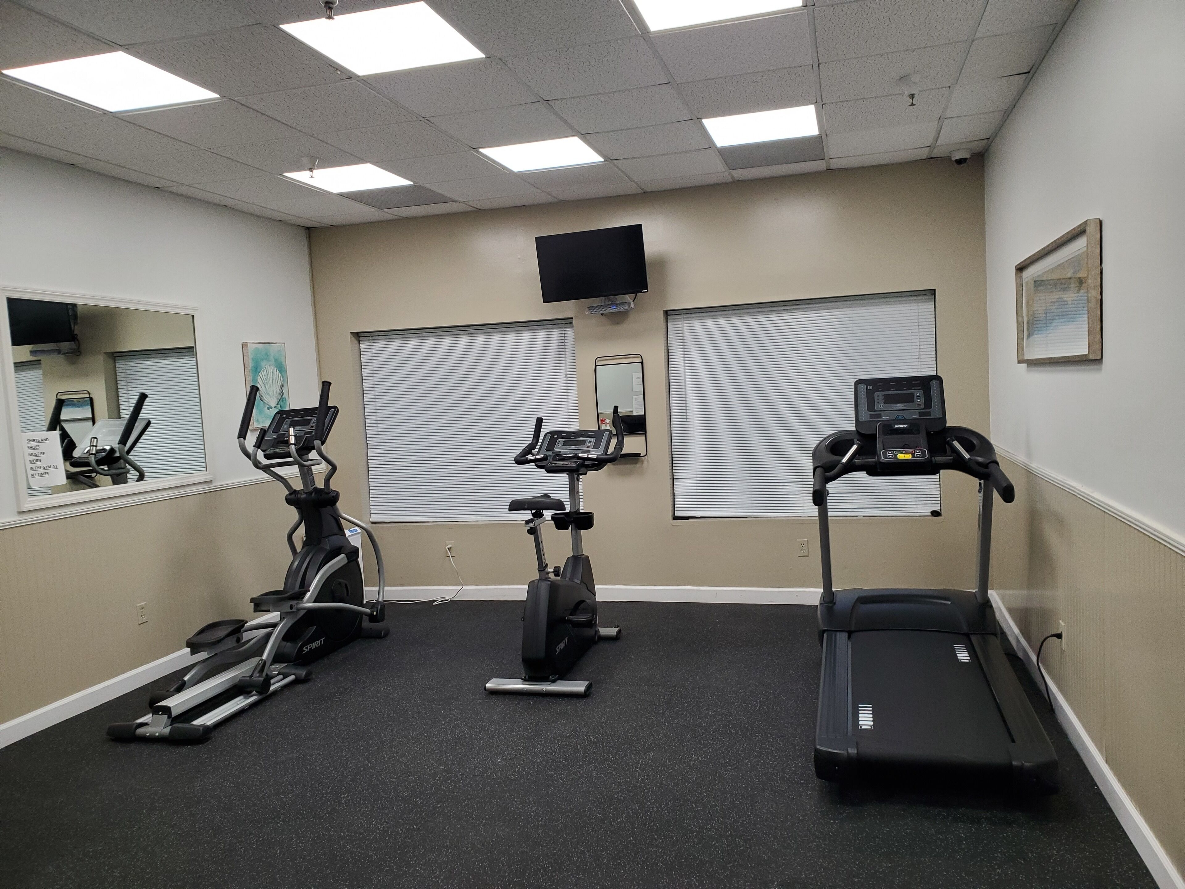 Un gimnasio con tres bicicletas estáticas, una cinta de correr y un espejo en la pared.