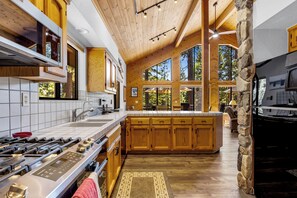 A spacious kitchen with a large island, wooden cabinets, and a stone accent wall. - Solitude in the Cedars, Spacious Mountain Home (Shaver Lake)
