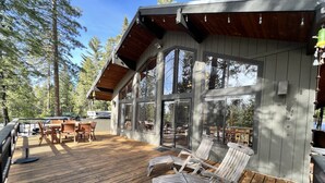 Una terraza de madera con muebles exteriores y ventanas amplias con vista a un área boscosa.
