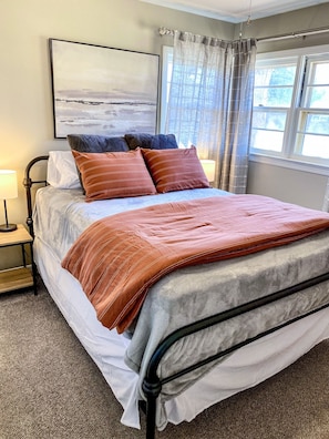 A neatly made bed with a patterned blanket and pillows, a bedside table with a lamp, and a window with curtains. - Updated 4 BR close to PDC & WTAMU (Canyon)