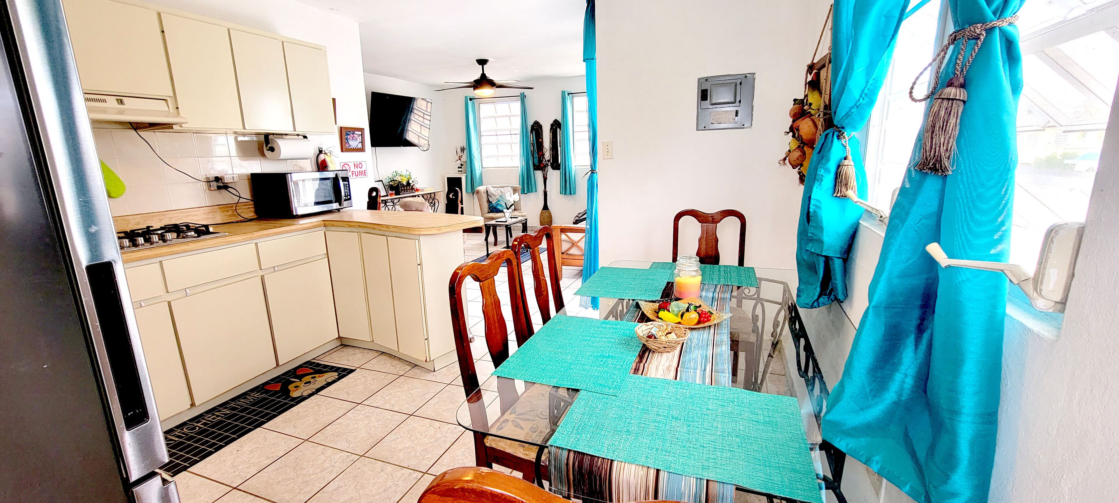 A compact kitchen with a microwave, stove, and cabinets. A dining table with chairs is set with a fruit bowl and placemats.