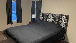 Quarto de hotel com uma cama grande, uma mesa de cabeceira com abajur e uma janela com cortinas.