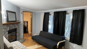 Uma sala de estar com lareira de pedra, um sofá, uma poltrona e uma janela com cortinas.