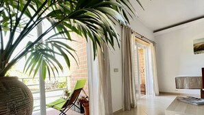 Um quarto iluminado com uma grande planta em vaso, uma cadeira verde e uma mesa de madeira.