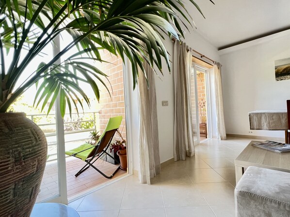 A bright room with a large potted plant, a green chair, and a wooden table.