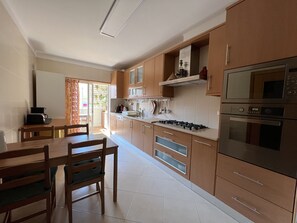 Uma cozinha moderna com armários de madeira, fogão a gás, forno e micro-ondas. Há uma mesa de jantar com cadeiras e uma janela com cortinas.