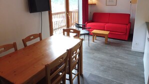 Un'area pranzo con un tavolo e sedie in legno, un divano rosso e una televisione a parete.