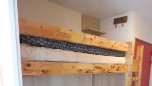 Un letto a castello con una scala in legno, un armadio e un piccolo ripiano sopra il letto.