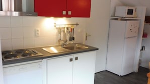 Una cucina con mobili bianchi, un pensile rosso, un lavello in acciaio inossidabile, un forno a microonde ed una lavastoviglie.