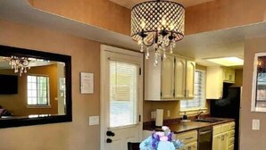 A dining area with a wooden table, four chairs, a chandelier, and a kitchen in the background. - Lovely Downtown Condo, Walk to Historic Downtown! (Flagstaff)
