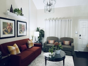 A living room with a red sofa, two armchairs, a glass coffee table, and a white door. - Pearlitah: Luxe 3BR King Ensuite, 4 Beds, Semi-Gated Central location (Greensboro)