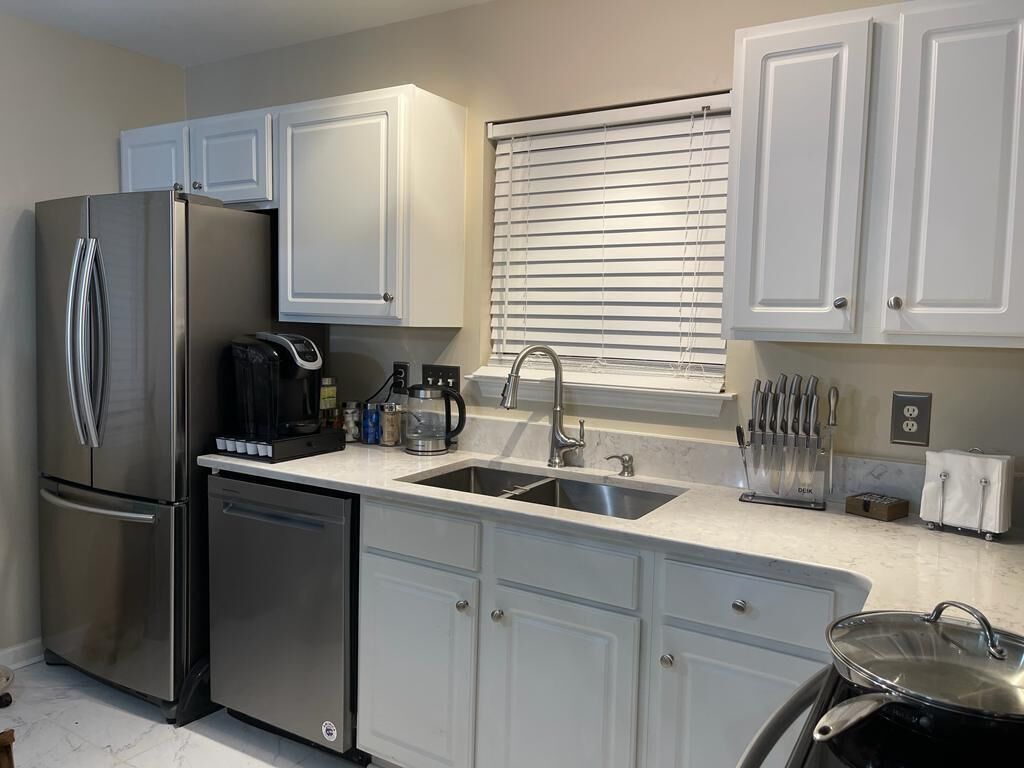 A modern kitchen with white cabinets, stainless steel appliances, a double sink, and a window with blinds.