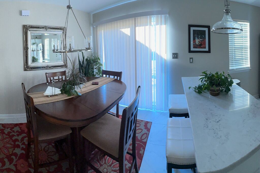 Comedor con mesa y sillas de madera, una isla de mármol blanco y un ventanal con persianas.