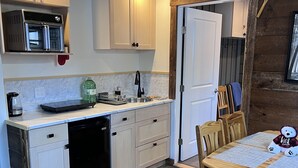 Une cuisine compacte avec des meubles blancs, un lave-vaisselle noir et une table à manger en bois avec des chaises.
