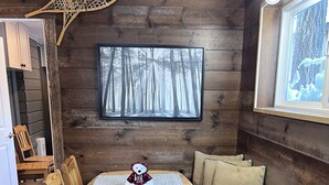 L’intérieur d’un chalet en bois chaleureux et accueillant, avec une table à manger, des chaises, un banc rembourré, un tableau représentant une forêt, et une tapisserie murale tissée.