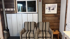 Un salon chaleureux avec un canapé à rayures, un mur en bois, une fenêtre et un tableau encadré.