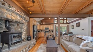Un intérieur chaleureux avec une cheminée en pierre, un plafond en bois, une cuisine avec des meubles en bois, un canapé et un coin repas.