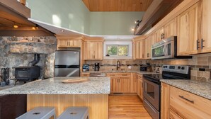 Une cuisine moderne avec des meubles en bois, des plans de travail en granit, une cheminée en pierre et des appareils électroménagers en acier inoxydable.