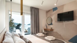 Une chambre d’hôtel moderne, dotée d’un grand lit, d’un téléviseur fixé au mur et offrant une vue sur la mer par la fenêtre.