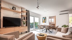 Un salon moderne doté d’un téléviseur à écran plat, d’étagères intégrées, d’un coin repas avec des chaises en osier et d’une grande porte-fenêtre coulissante donnant sur un balcon.